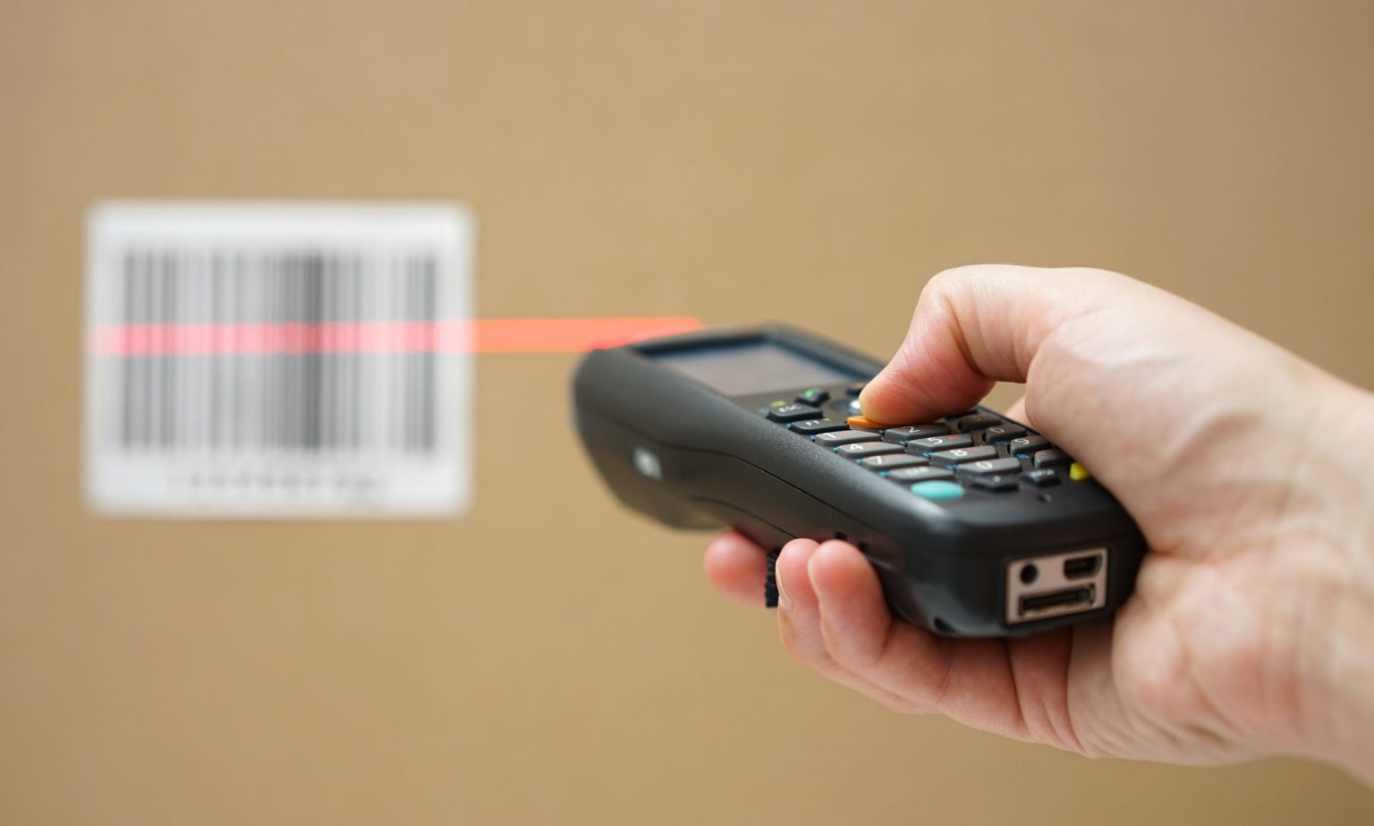 closeup of hand holding bar code scanner and scanning code on cardboard box