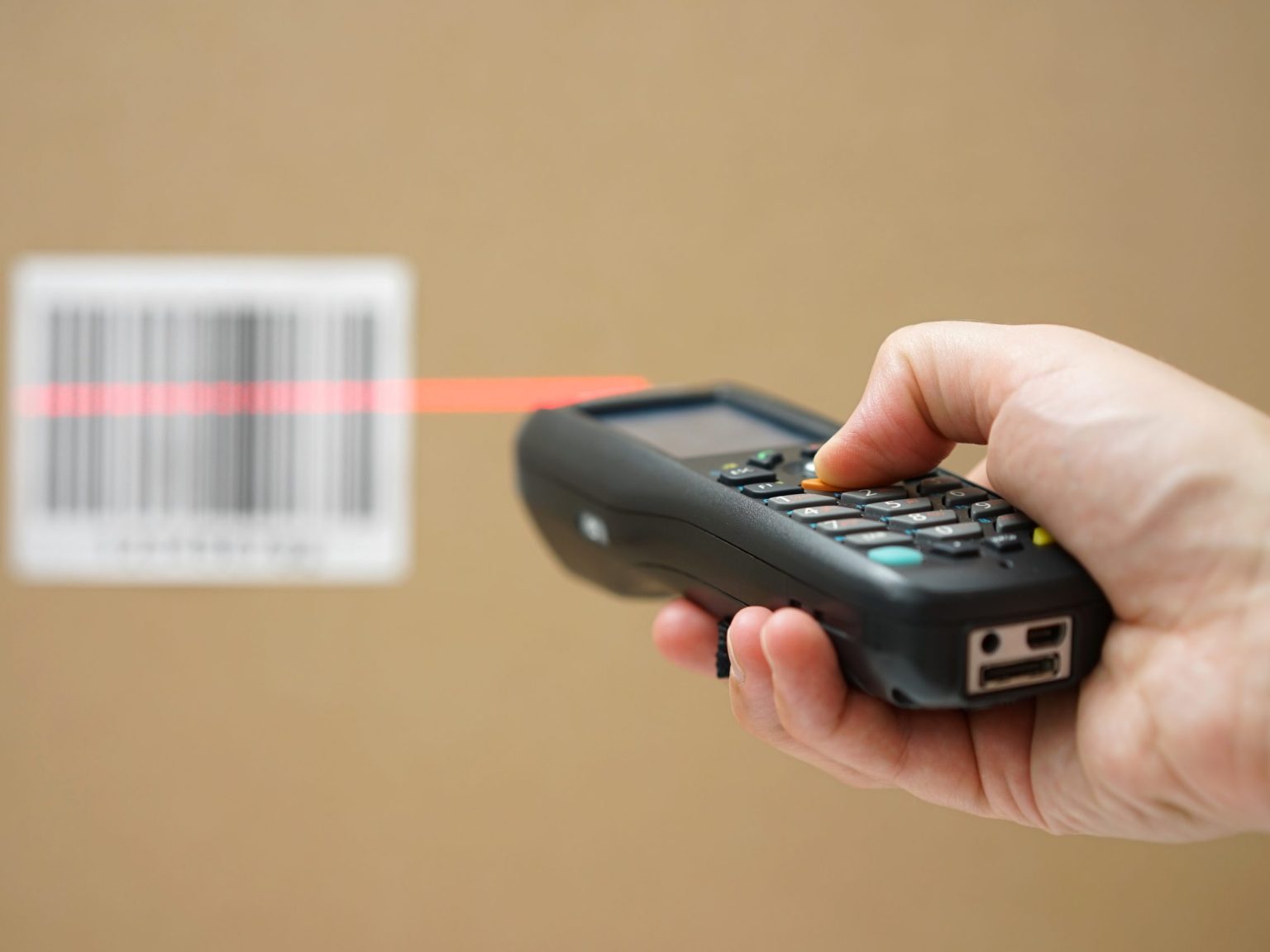 closeup of hand holding bar code scanner and scanning code on cardboard box